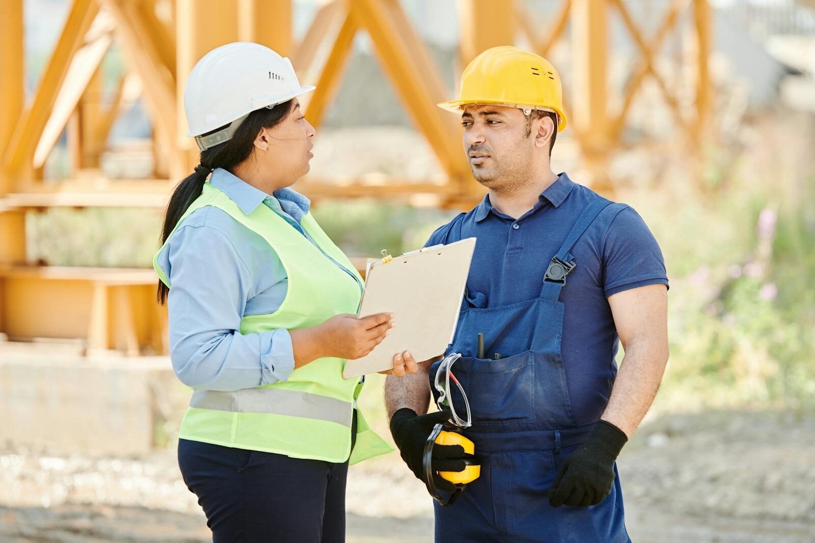 Male and female construction workers talking with safety gear at an outdoor site.